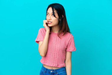 Mavi arka planda izole edilmiş genç Vietnamlı kadın biraz gergin.