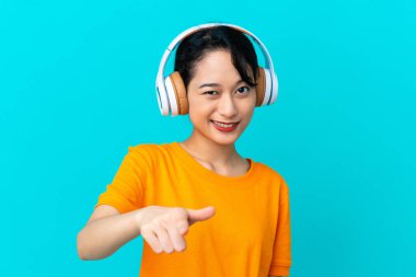 Genç Vietnamlı kadın mavi arka planda izole edilmiş müzik dinliyor.