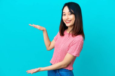 Genç Vietnamlı bir kadın, mavi arka planda izole edilmiş bir ilan vermek için kopyalama alanı tutuyor.