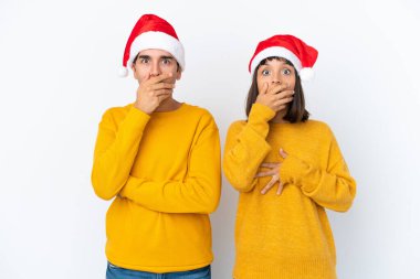 Genç melez çift, Noel 'i beyaz arka planda izole edilmiş bir şekilde kutluyor. Ağızlarını uygunsuz bir şey söyledikleri için elleriyle kapatıyor.