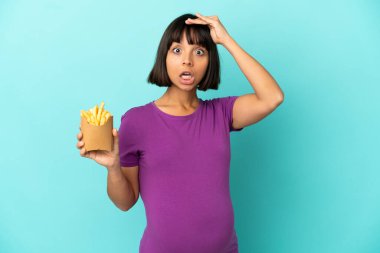 Hamile bir kadın izole edilmiş arka planda patates kızartması tutuyor. Yan tarafa bakarken sürpriz jest yapıyor.