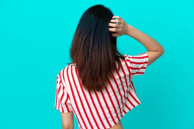 Genç Vietnamlı kadın mavi arka planda izole edilmiş ve düşünüyor.