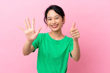 Pembe arka planda izole edilmiş genç Vietnamlı kadın parmaklarıyla altısını sayıyor.