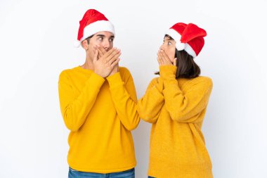 Genç melez çift, Noel 'i beyaz arka planda izole edilmiş bir şekilde kutluyor. Ağızlarını uygunsuz bir şey söyledikleri için elleriyle kapatıyor.