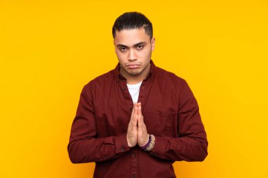 Asyalı yakışıklı adam sarı arka planda izole edilmiş ve en iyinin işareti olarak parmağını kaldırıyor.