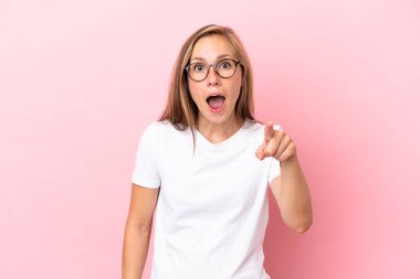 Pembe arka planda izole edilmiş genç İngiliz kadın şaşırmış ve ön tarafı işaret ediyor.