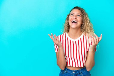 Mavi arka planda izole edilmiş kıvırcık saçlı kız çok gülümsüyor.