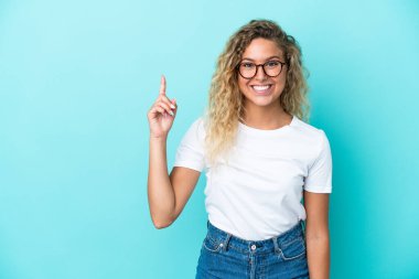 Mavi arka planda izole edilmiş kıvırcık saçlı kız harika bir fikre işaret ediyor.