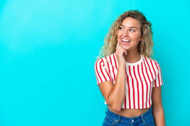 Kıvırcık saçlı kız mavi arka planda izole edilmiş bir şekilde yukarı bakarken bir fikir düşünüyor.