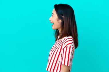 Genç Vietnamlı kadın mavi arka planda izole edilmiş. Yan pozisyonda gülüyor.