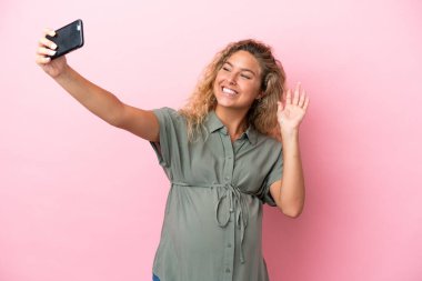Kıvırcık saçlı kız pembe arka planda izole edilmiş hamile ve selfie çekiyor.