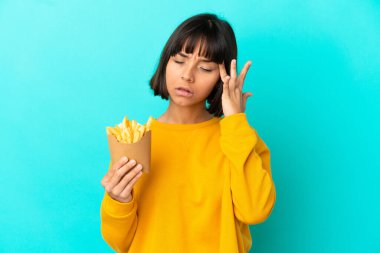 Genç esmer kadın elinde kızarmış cipslerle izole edilmiş mavi arka planda baş ağrısı çekiyor.