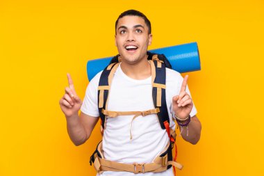 Sarı arka planda izole edilmiş büyük sırt çantalı genç dağcı Asyalı adam işaret parmağıyla işaret etmek harika bir fikir.