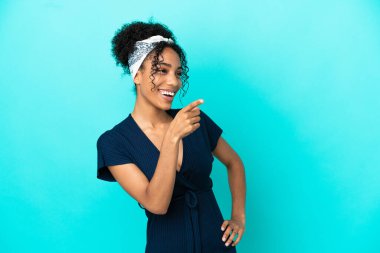 Mavi arka planda izole edilmiş genç Latin bir kadın parmak göstererek bir ürün sunuyor.