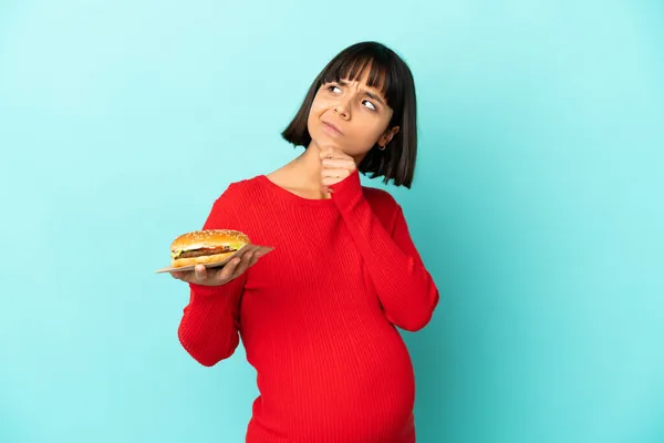 Mujer Embarazada Joven Sosteniendo Una Hamburguesa Sobre Fondo Aislado Mirando — Foto de Stock