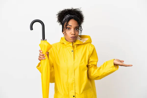 手を上げながら疑問を持ちながら白い背景に隔離されたレインプルーフコートと傘を持つ若い女性 — ストック写真
