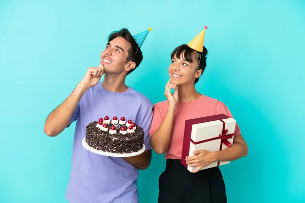 年轻的混血种族夫妇手握生日蛋糕 带着蓝色背景的孤身一人 一边举目一边想办法 — 图库照片