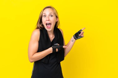 Beyaz arka planda izole edilmiş genç İngiliz kadın şaşırmış ve işaret ediyor.