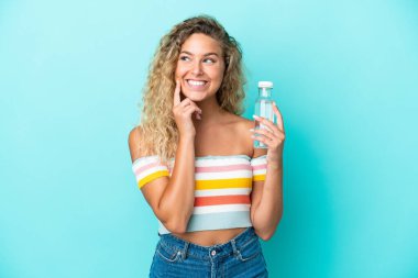 Mavi arka planda bir şişe suyu olan genç sarışın kadın yukarı bakarken bir fikir düşünüyor.