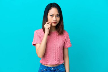 Mavi arka planda izole edilmiş genç Vietnamlı kadın sessizlik işareti gösteriyor.