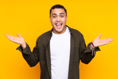 Asyalı yakışıklı adam sarı arka planda izole edilmiş, şaşırmış ve işaret ediyor.