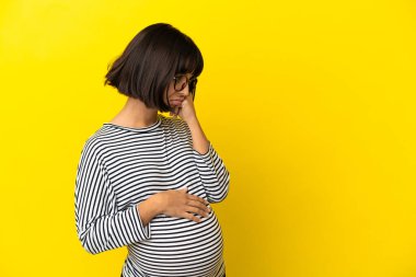 Genç hamile kadın, izole edilmiş sarı arka planda yorgun ve sıkılmış bir ifadeyle