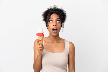 Beyaz arka planda izole edilmiş kornet dondurmalı genç Afro-Amerikalı kadın yukarı bakıyor ve şaşırmış bir ifadeyle