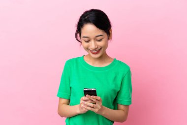 Pembe arka planda izole edilmiş genç Vietnamlı kadın cep telefonuyla mesaj gönderiyor.