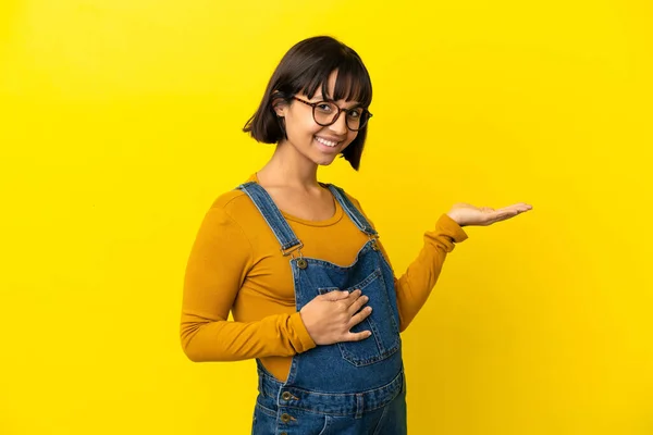 若いです妊娠中の女性以上隔離された黄色の背景保持コピースペース想像上のザ手のひらに挿入する広告 — ストック写真