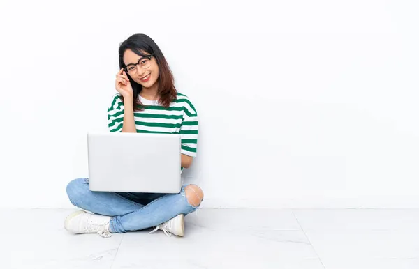 年轻的越南妇女 带着笔记本电脑坐在地板上 隔离在白墙上 戴着眼镜 快乐极了 — 图库照片