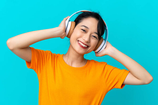 Young Vietnamese woman isolated on blue background listening music