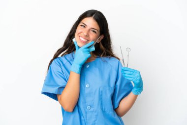 Dişçi kadın beyaz arka planda aletleri tutuyor. Mutlu ve gülümsüyor.