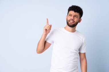 Faslı genç bir adam mavi arka planda izole edilmiş yukarı bakıyor ve şaşırıyor.