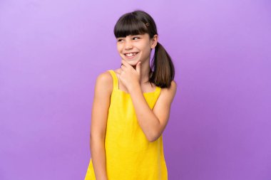 Mor arka planda izole edilmiş küçük beyaz çocuk yana bakıyor ve gülümsüyor.