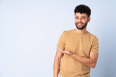 Faslı genç bir adam mavi arka planda izole edilmiş bir şekilde gülümserken bir fikir sunuyor.