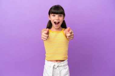 Mor arka planda izole edilmiş küçük beyaz çocuk şaşırmış ve ön tarafı işaret ediyor.