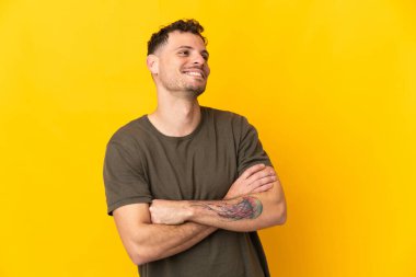 Sarı arka planda izole edilmiş genç beyaz yakışıklı adam mutlu ve gülümsüyor.