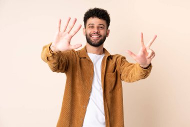 Faslı genç bir adam bej arka planda izole edilmiş. Sekiz parmaklı sayıyor.