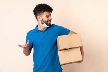 Genç teslimatçı Faslı adam bej arka planda izole edilmiş ve yüzünde sürpriz bir ifade var.