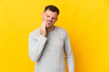 Sarı arka planda dişleri ağrıyan beyaz, yakışıklı genç bir adam.
