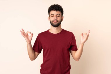 Faslı genç bir adam Zen pozunda bej arka planda izole edilmiş.