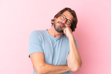 Yaşlı Hollandalı adam pembe arka planda izole edilmiş gözlüklü ve üzgün bir ifadeyle