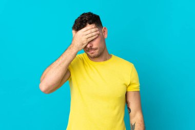 Kafkasyalı yakışıklı genç adam mavi arka planda başağrısı ile izole edilmiş.