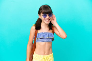 Küçük beyaz bir çocuk kumsala gidiyor. Mavi arka planda izole edilmiş bir şekilde. Kulağına elini sürerek bir şeyler dinliyor.