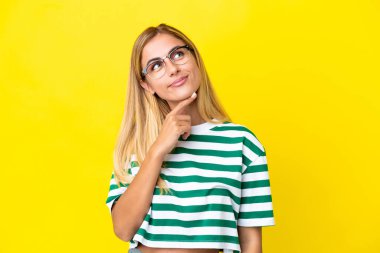 Sarışın Uruguaylı kız sarı arka planda izole edilmiş gülümserken yukarı bakıyor