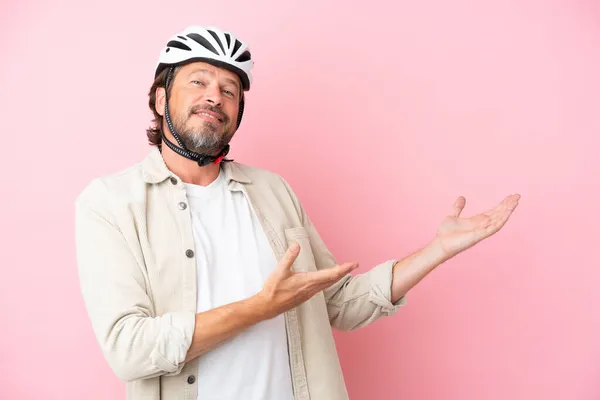 シニアオランダ人男とともにバイクヘルメット隔離でピンクの背景拡張手に側に招待するために来る — ストック写真