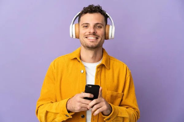 若いですCaucasianハンサムな男絶縁上の紫背景リスニング音楽とともにモバイルと見てフロント — ストック写真