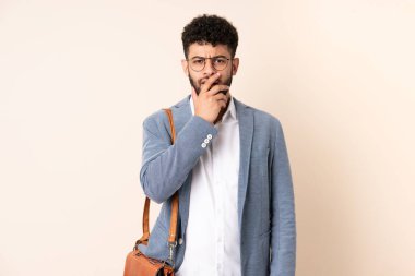 Faslı genç bir iş adamı bej arka planda izole edilmiş, şaşırmış ve şaşırmış görünüyor.