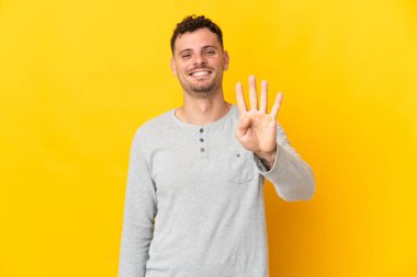 Sarı arka planda izole edilmiş beyaz, yakışıklı genç bir adam mutlu ve parmaklarıyla dört kişi sayıyor.