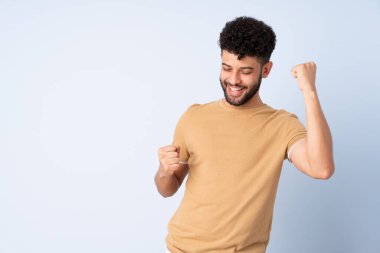 Genç Faslı bir adam mavi arka planda izole edilmiş zaferi kutluyor.